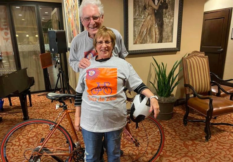 An older couple smiling while posing with a bike, enjoying a leisurely ride together.