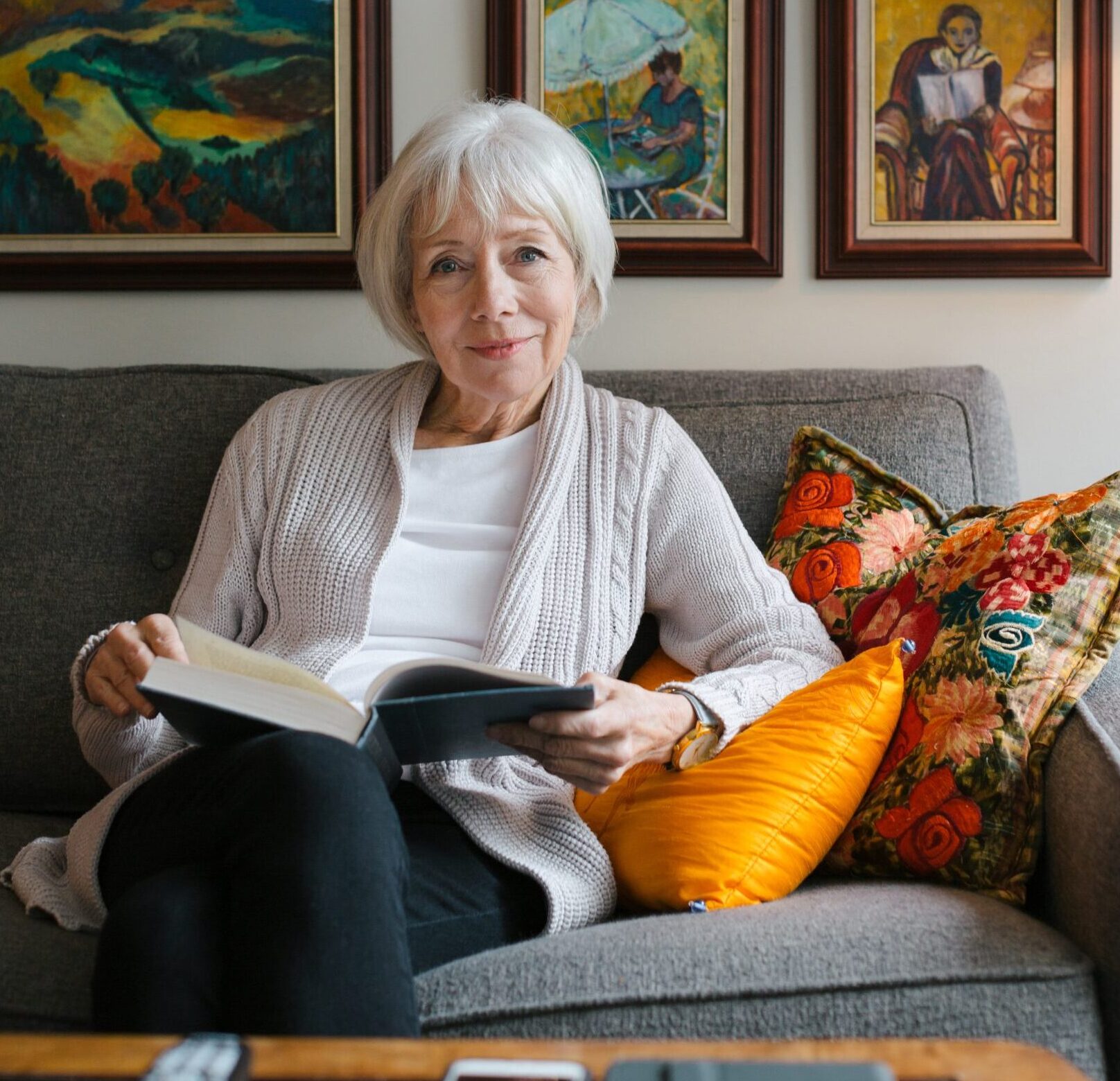 an elderly woman reading with beautiful paintings behind her