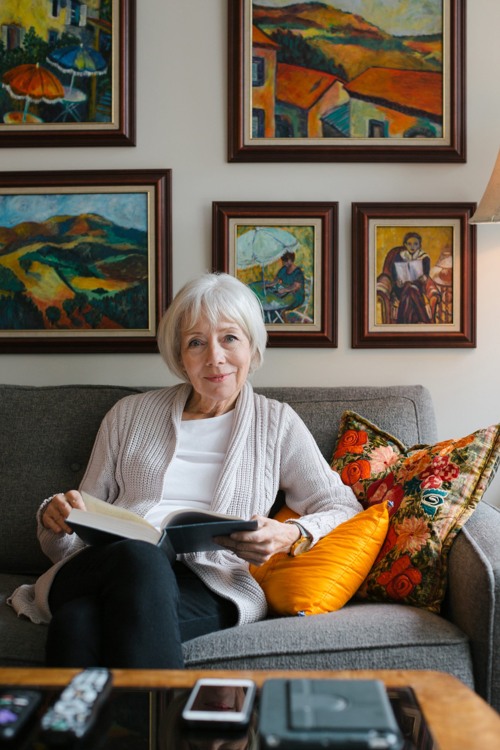 an elderly woman reading with beautiful paintings behind her