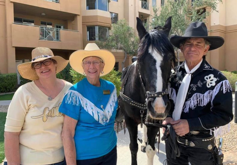 Two individuals wearing cowboy hats stand beside a horse, striking a pose.