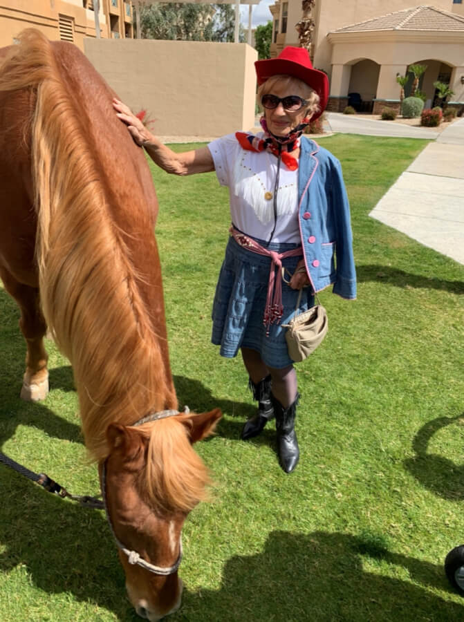 A woman in a cowboy hat and dress standing next to a horse, exuding a sense of Western charm and elegance.