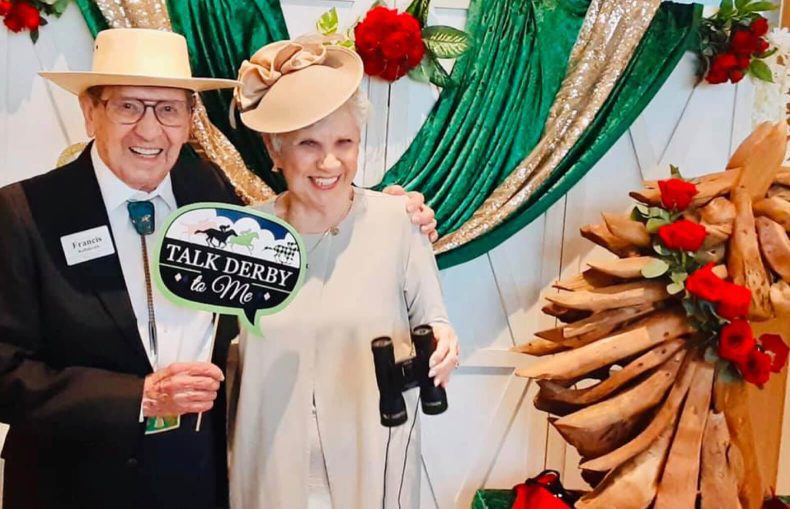 An older couple smiling and holding a sign while posing for a photo together.