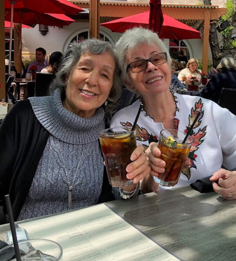 Two elderly women enjoying drinks while sitting at a table.