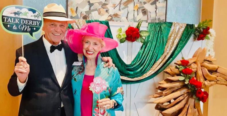 An older couple smiling and holding a sign while posing for a photo together.