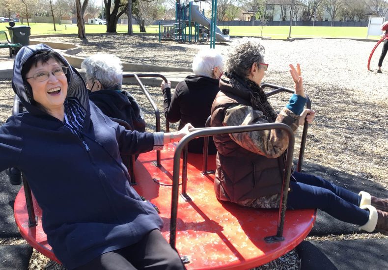 Two women enjoying a merry-go-round ride at a playground, filled with laughter and joy.