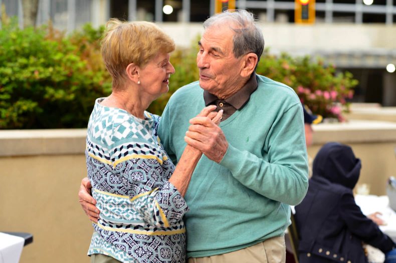 An older couple gracefully dancing outdoors at an event, radiating joy and love through their movements.