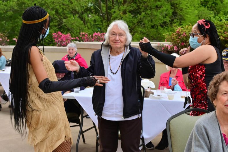 A woman in a vibrant costume joyfully dances alongside a group of people, exuding energy and enthusiasm.