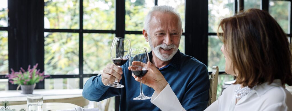 An elderly couple celebrating with wine at a restaurant, raising their glasses in a toast.