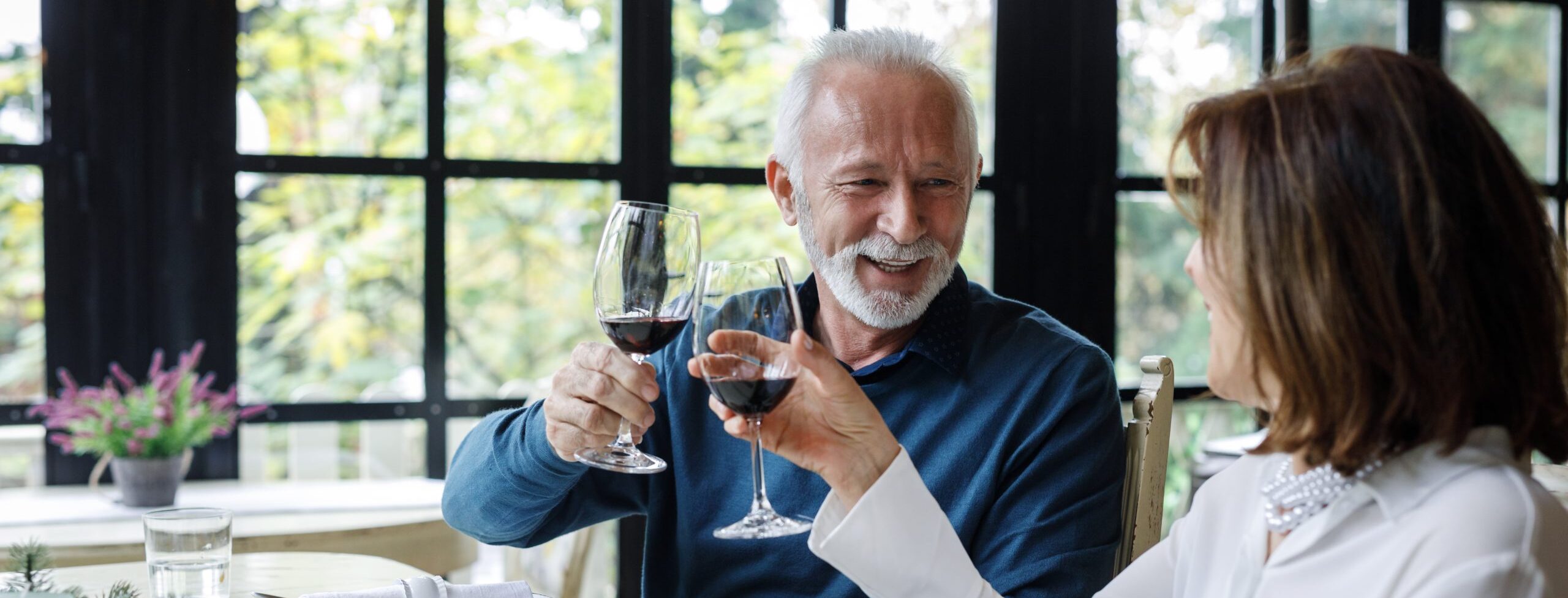 An elderly couple celebrating with wine at a restaurant, raising their glasses in a toast.