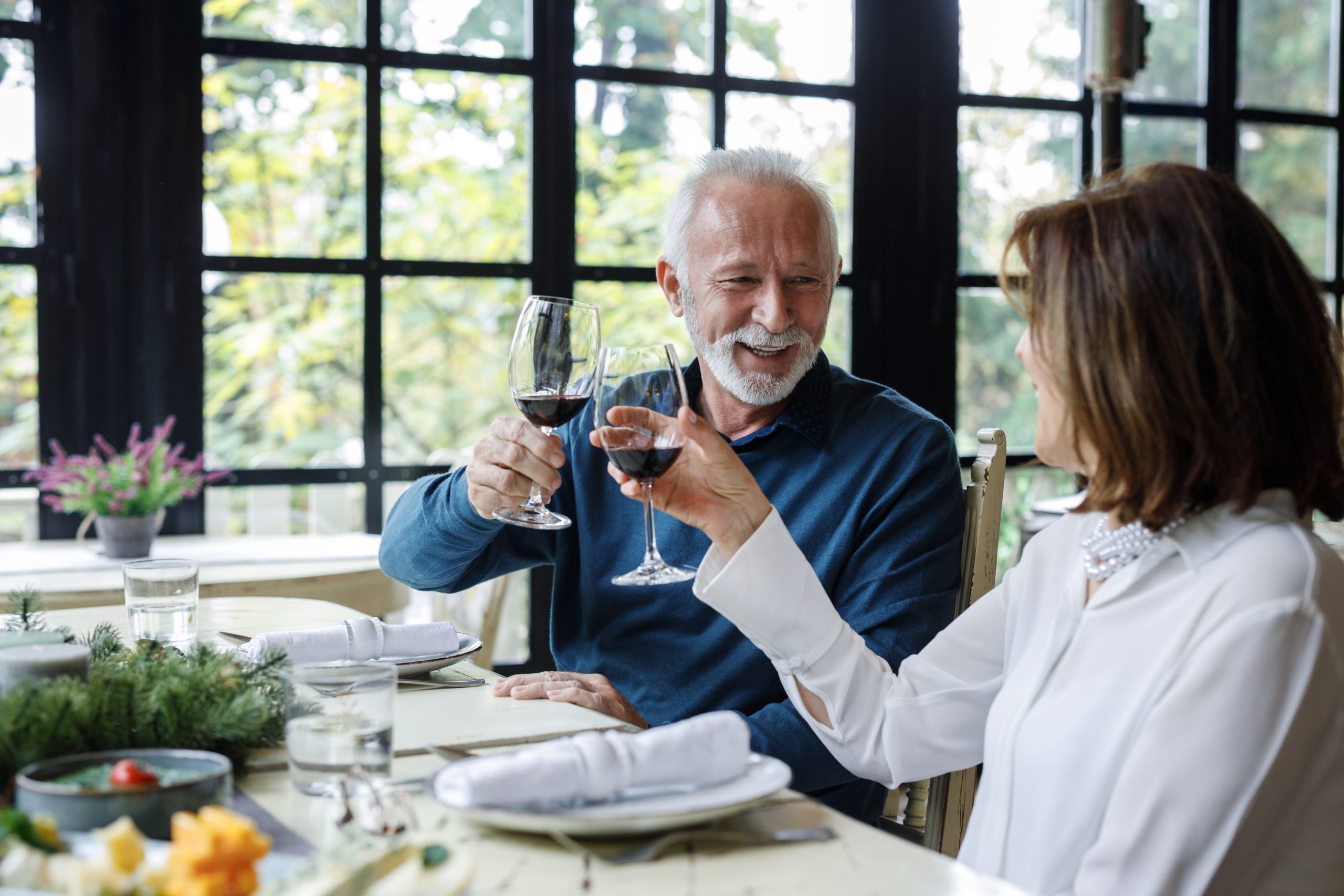 An elderly couple celebrating with wine at a restaurant, raising their glasses in a toast