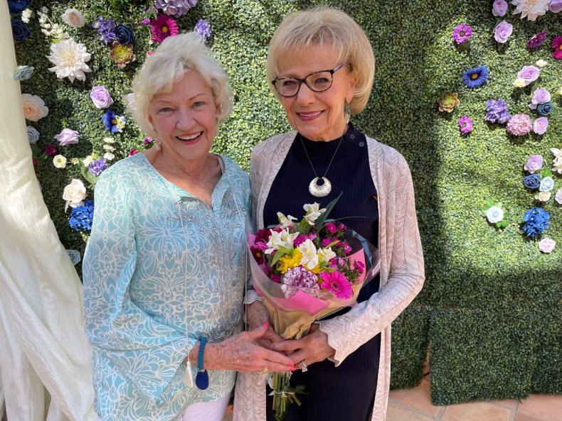 Two elderly women smiling and holding bouquets of flowers in their hands.