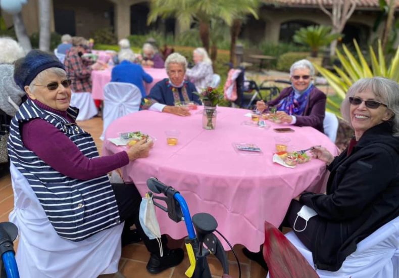 A group of women sitting at a table with pink tablecloths, engaged in conversation and enjoying each other's company.