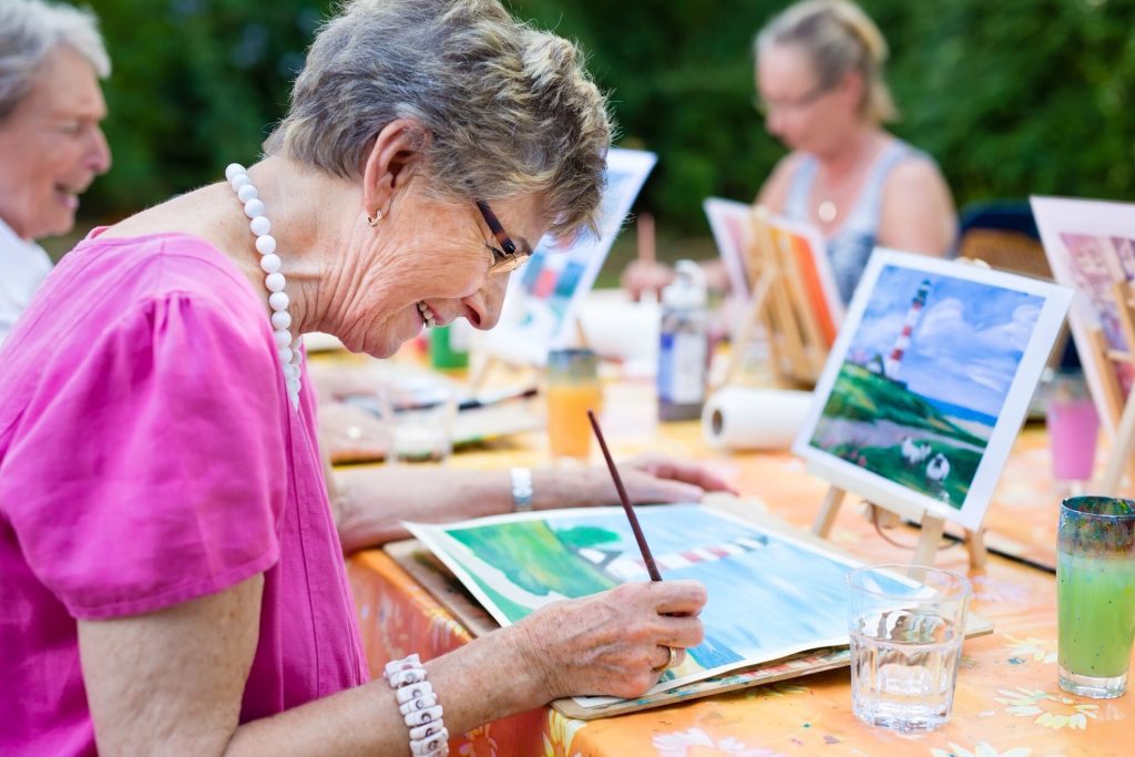 An elderly woman passionately painting a beautiful artwork at an outdoor event.