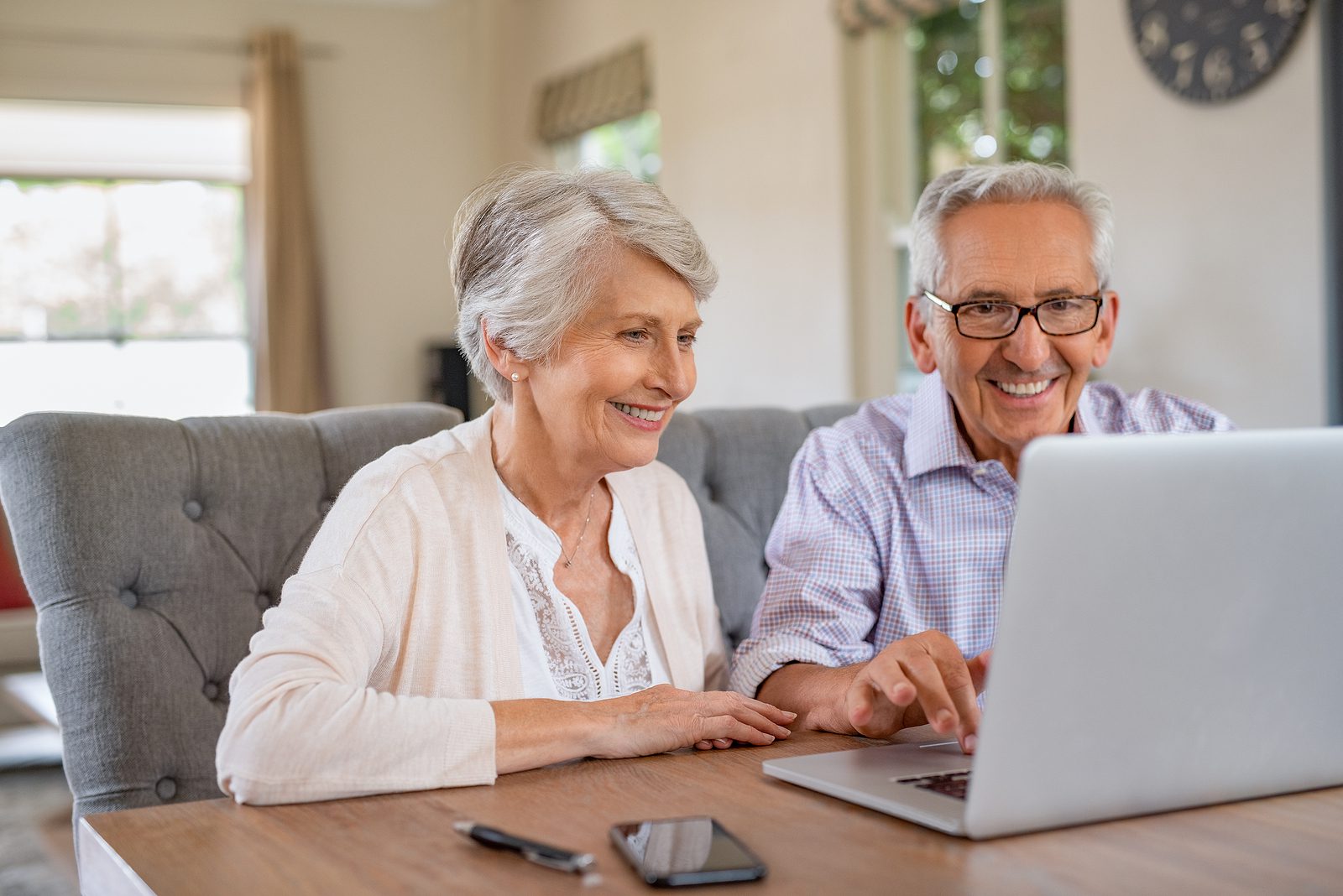 Senior couple sits at a table and talks with family via video call on a laptop