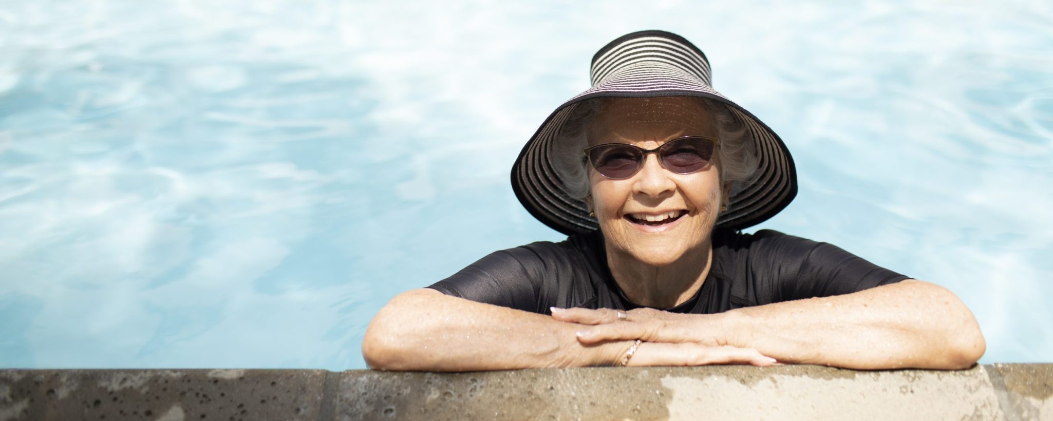 An elderly woman enjoying the pool donning a stylish hat and sunglasses for protection from the sun s rays 