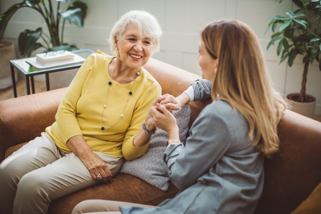 A woman conversing with an elderly woman on a couch.