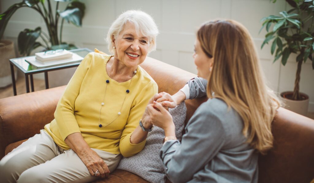 Senior woman smiling while talking with caregiver indoors.