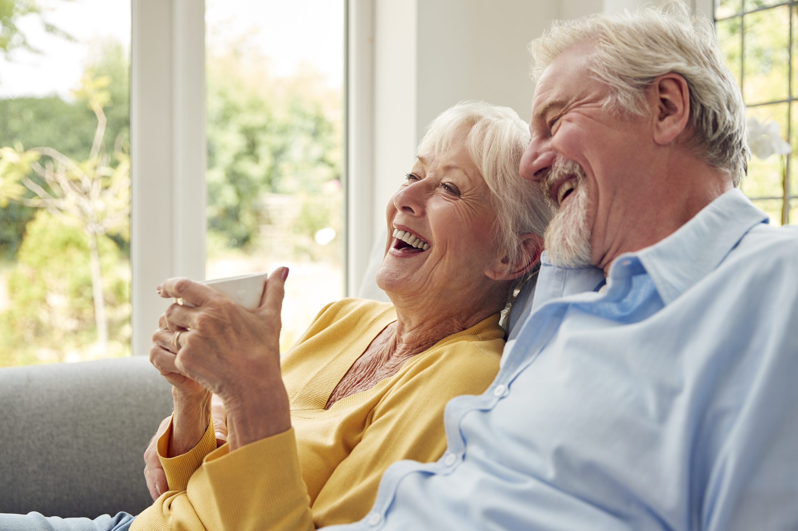 An older couple sharing a joyful moment, sitting on a couch and laughing together.