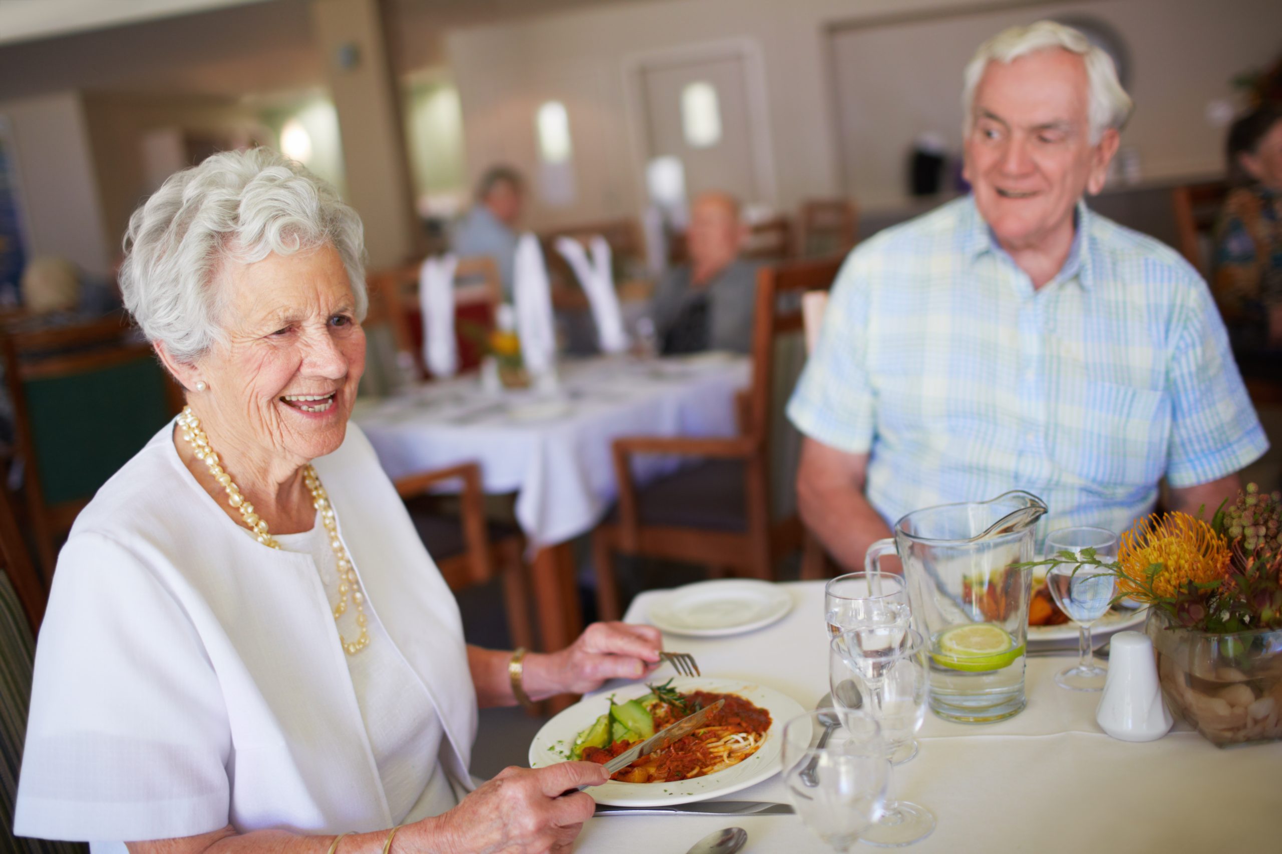 two elderly people eating spaghetti for dinner and talking to each other