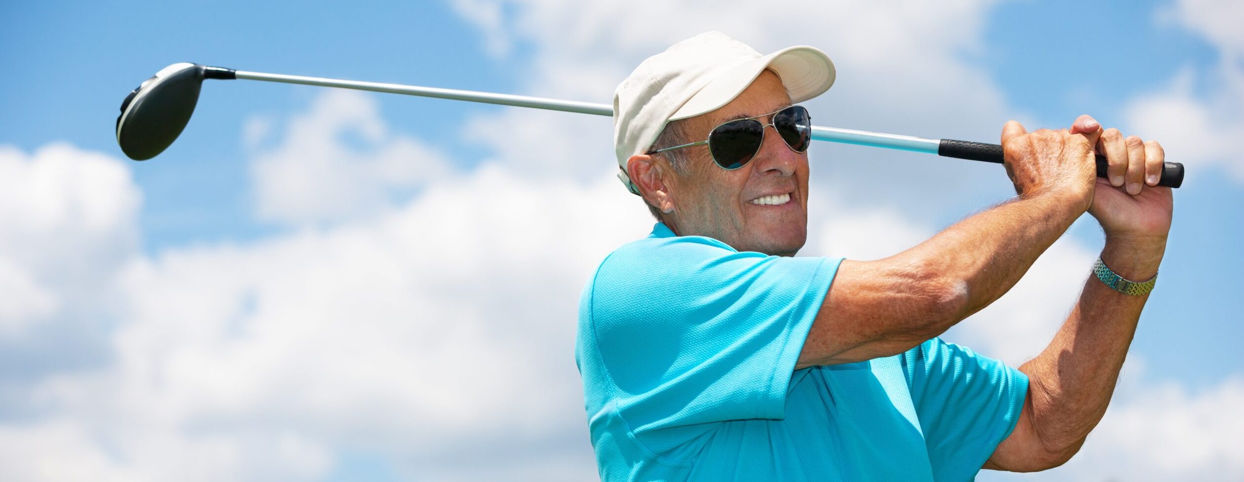 active elderly man playing golf with sunglasses smiling after a good shot on the green