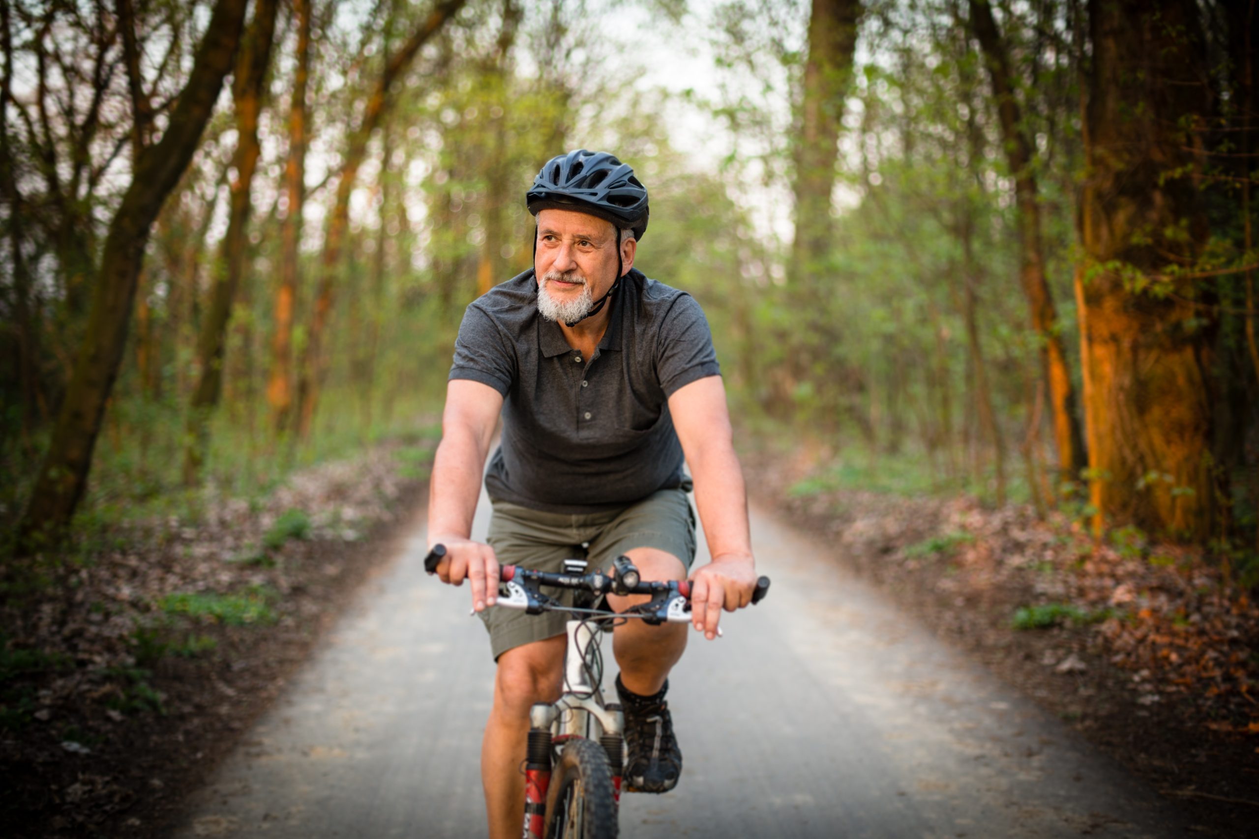 elderly man smiling while riding a bike and wearing a helmet