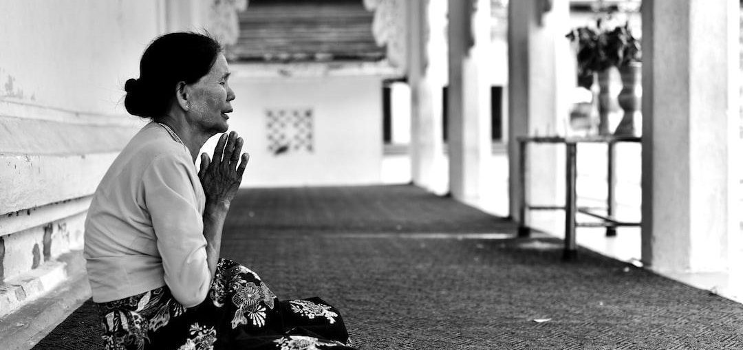 A woman sitting on the floor, deep in prayer, with her eyes closed and hands clasped together.