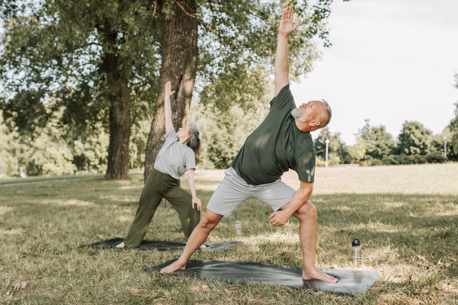 two elderly people doing yoga together outside on mats