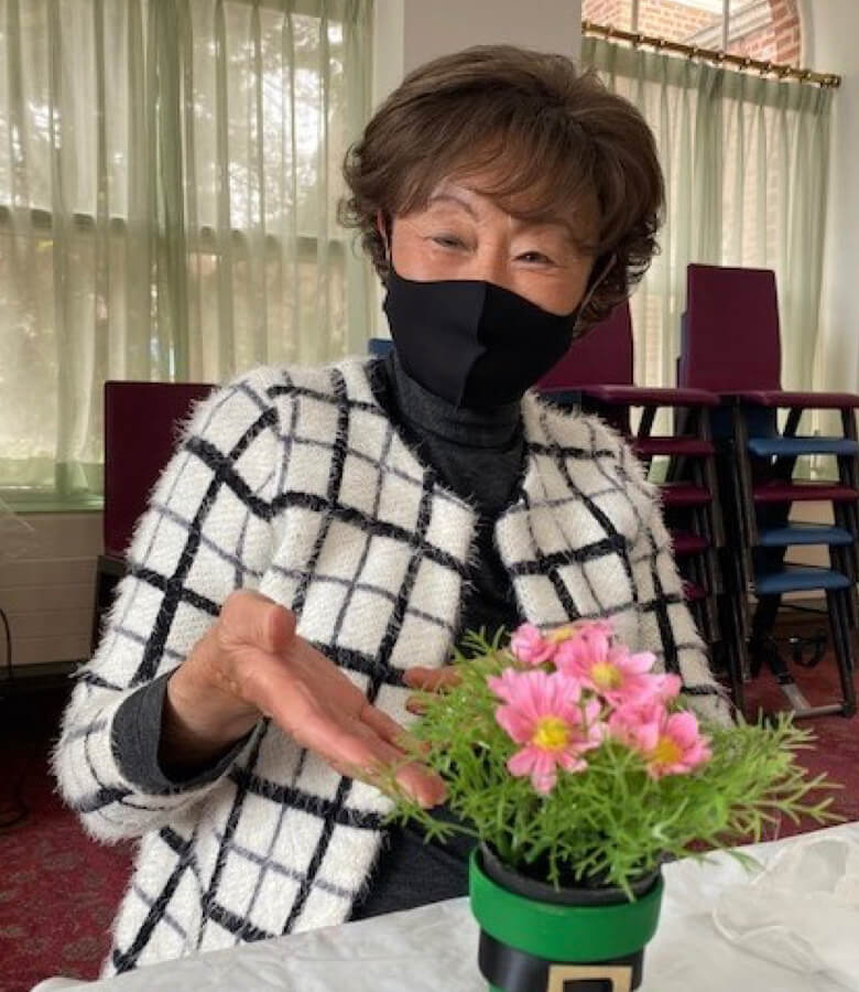 A woman wearing a face mask holds a flower pot, showcasing her care for both her health and the beauty of nature.