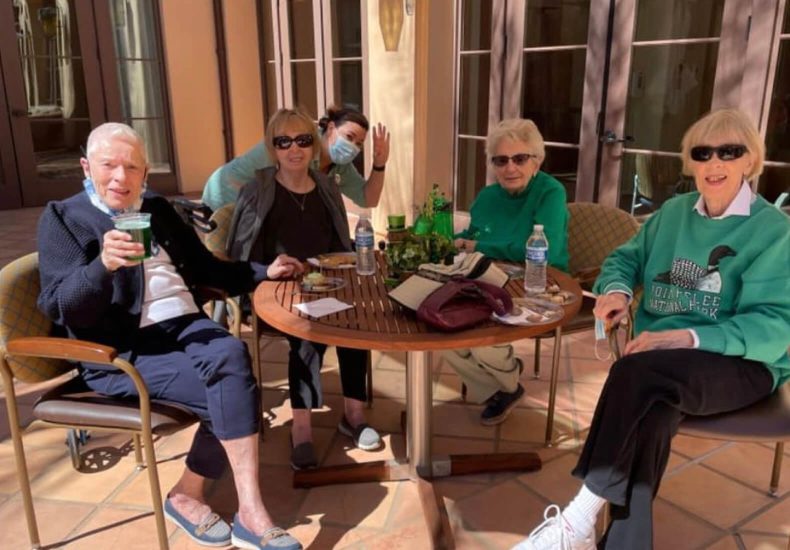 Four older women enjoying drinks at a table, engaged in conversation and sharing laughter.
