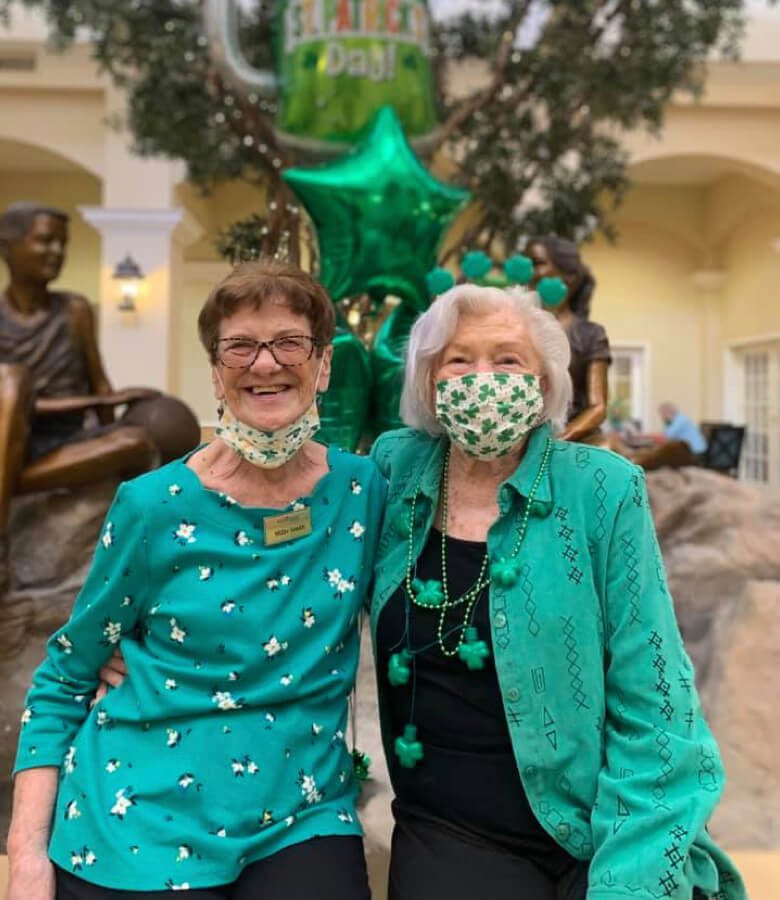 Two elderly women wearing green face masks for st patricks day protecting themselves and others from potential health risks.