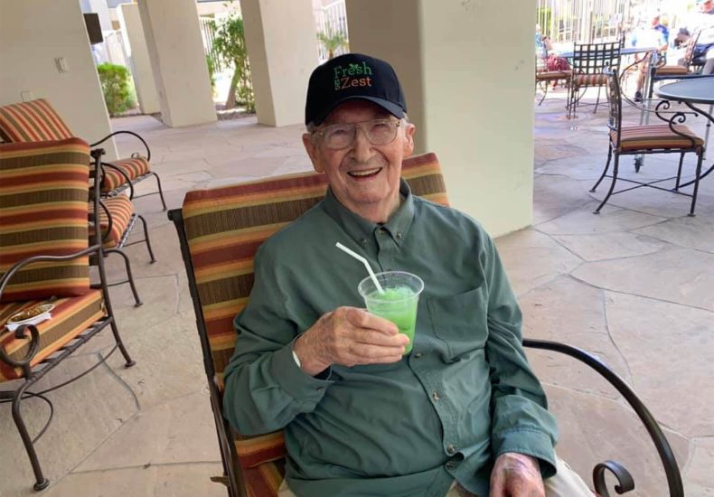 An elderly man enjoying a beverage while seated in a chair.