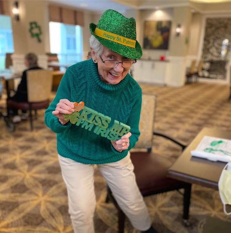 An elderly woman in a green hat holds a sign saying 