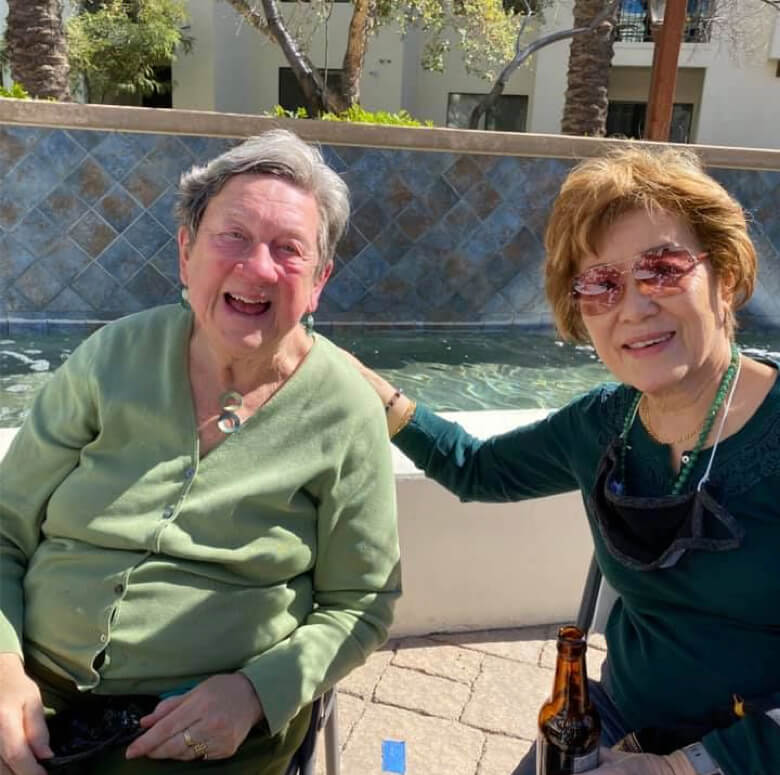 Two elderly women enjoying a poolside moment, sitting on chairs and basking in the sun's warmth.