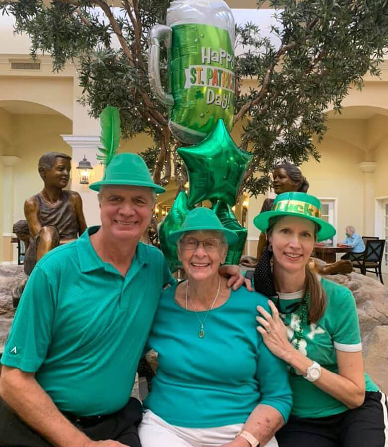 Three people in green shirts and hats smiling for a photo.