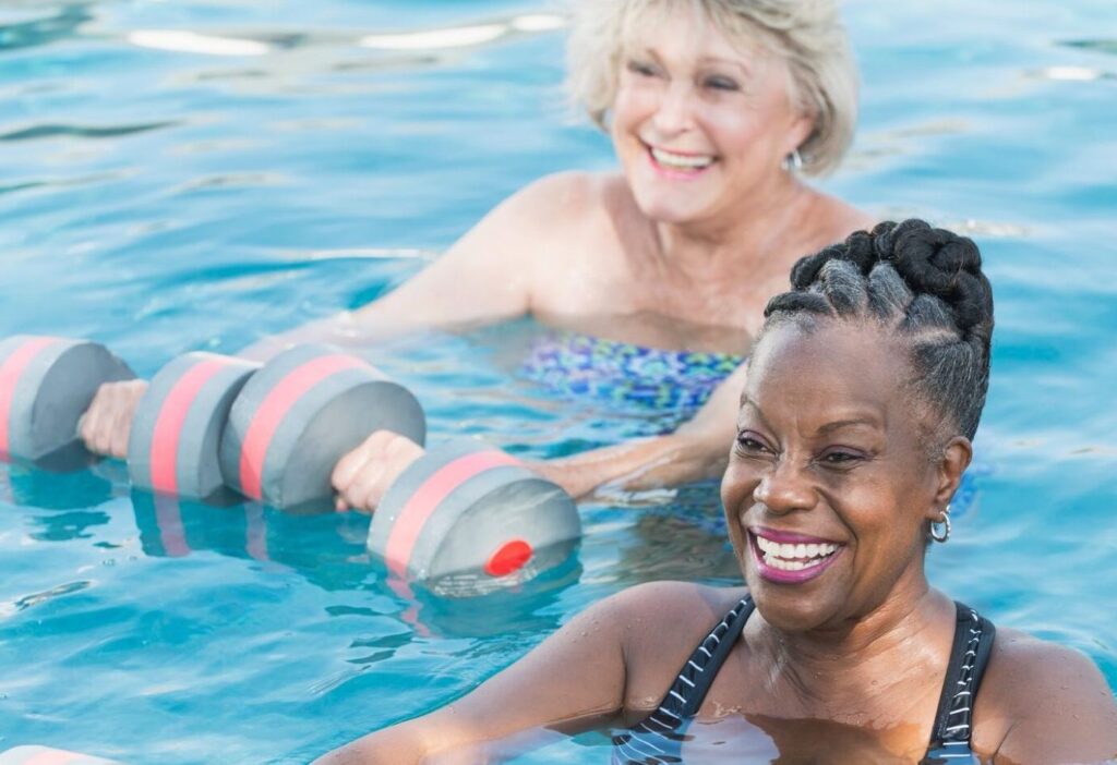 Two women exercising in a pool with dumbbells, promoting fitness and strength training in a refreshing aquatic environment.