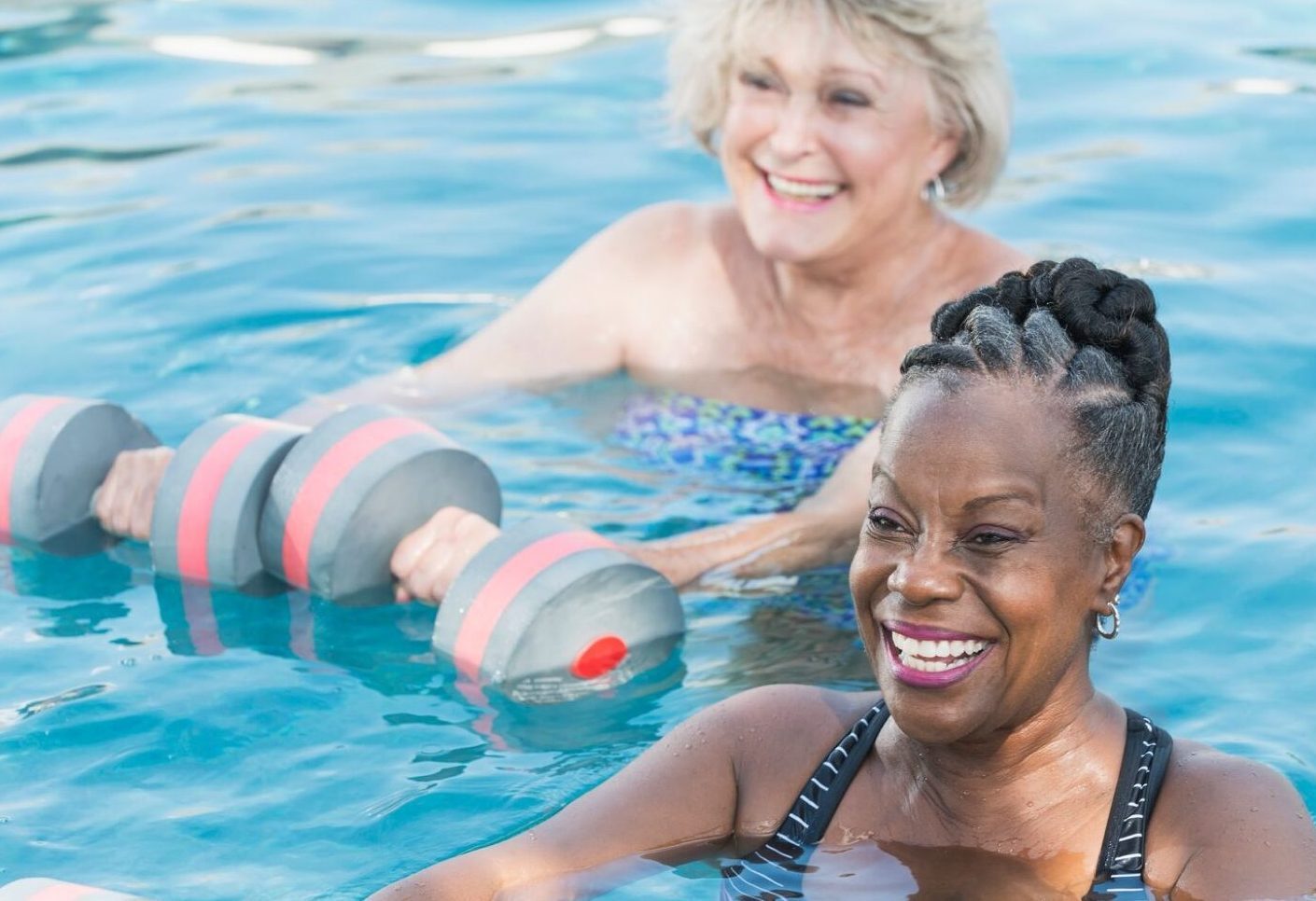 Two women exercising in a pool with dumbbells, promoting fitness and strength training in a refreshing aquatic environment.