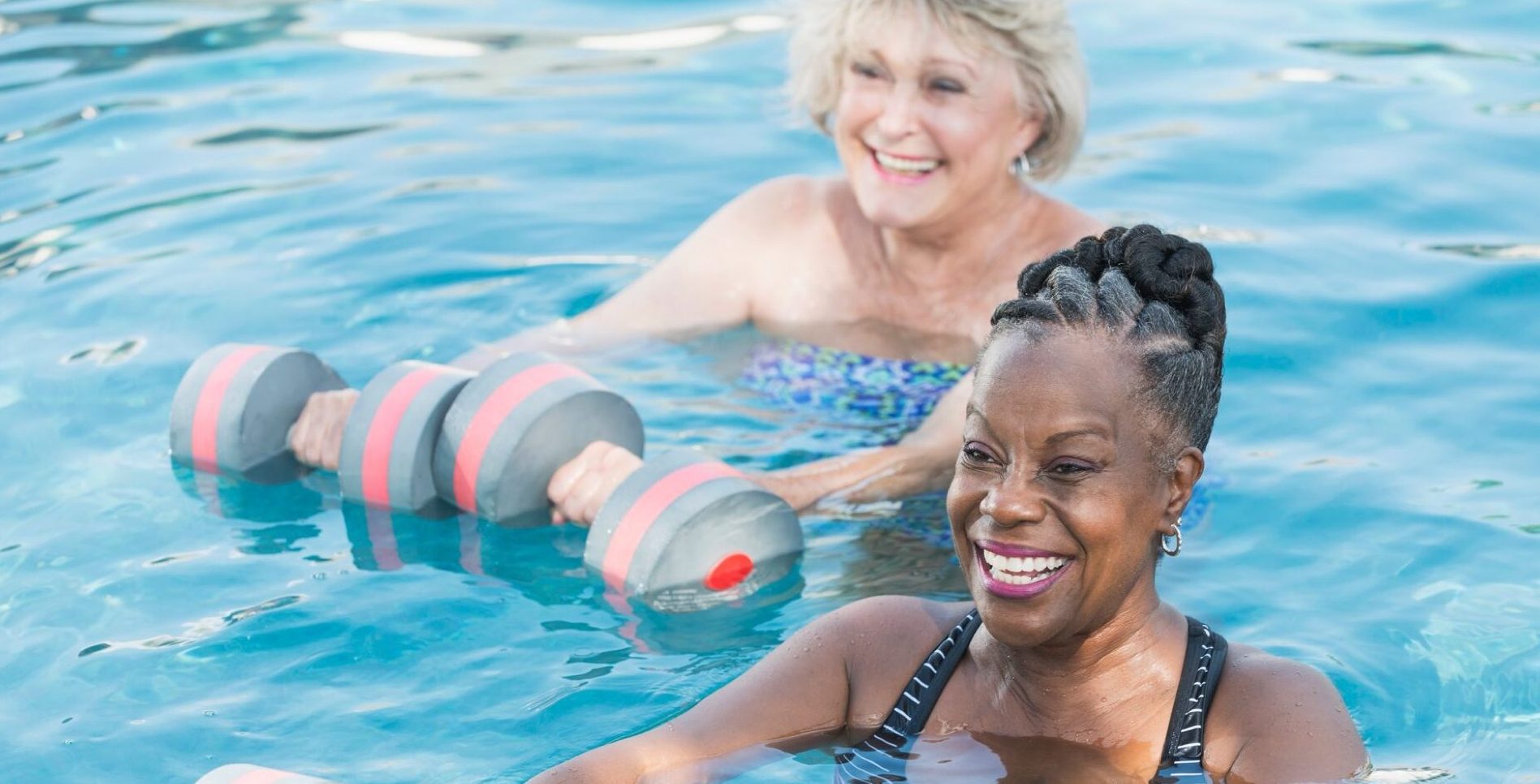 Two women exercising in a pool with dumbbells, promoting fitness and strength training in a refreshing aquatic environment.